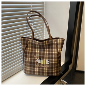 Detail of plaid tote bag with dog embroidery and leather handles on a windowsill