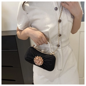 Détail d'une pochette de soirée noire avec boucle florale en strass et chaîne dorée