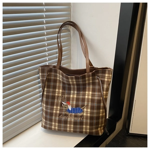 Detail of a brown plaid tote bag featuring a cute dog embroidery and a side metal zipper