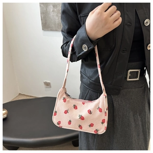 Détail d'un sac sous le bras en velours rose avec imprimé fraise porté sur une veste
