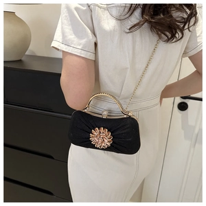 Détail de la pochette de soirée noire avec fleur en cristal et chaîne dorée sur tenue