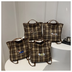 Detail of four brown plaid tote bags with colorful dachshund embroidery on a white display