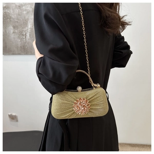 Détail de pochette de soirée dorée à paillettes avec fleur en strass et poignée en métal