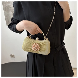 Détail d'une pochette dorée plissée avec fleur en strass et bandoulière chaîne amovible
