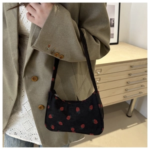 Détail d'un sac d'épaule en velours côtelé noir avec imprimé fraise porté par un mannequin
