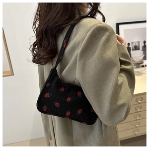 Détail d'un sac sous le bras en velours noir avec broderie de fraises rouges