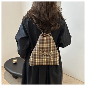Close-up of checkered backpack featuring a cartoon dachshund embroidery and drawstring detail