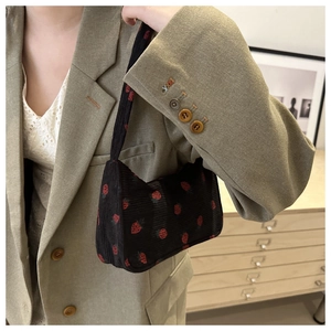 Détail du sac bandoulière en velours côtelé noir avec motif fraise sur un costume vert