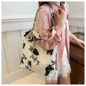 Close-up of black butterfly embroidery on an off-white canvas tote bag with floral patterns