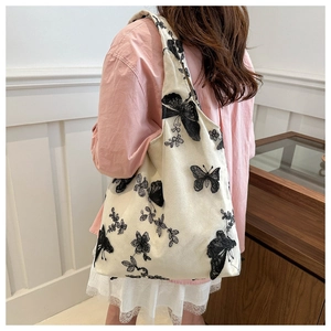 Detailed embroidery of butterfly on cream chiffon tote bag worn by a female model