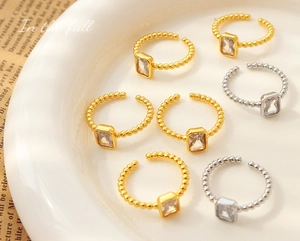 Close-up of gold and silver beaded open rings featuring a rectangular zircon stone