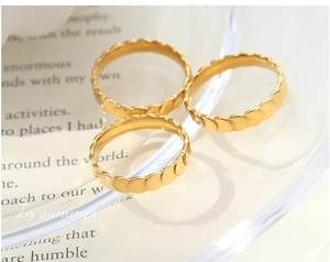 Detailed view of three gold-plated wave-textured rings on a glass tray with paper