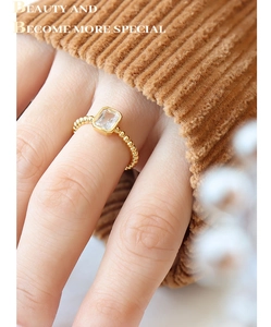 Close-up of a gold-plated beaded ring with a rectangular clear zircon on a finger