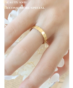 Detailed view of a gold-plated scalloped sequin ring worn on a finger with a floral background