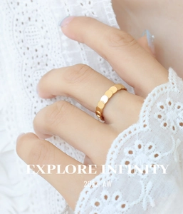 Close-up of golden scale-layered minimalist ring worn on finger with lace background