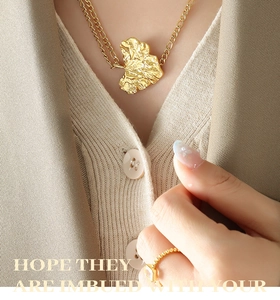 Detalle de collar doble dorado con hoja de ginkgo y anillo con gema cuadrada