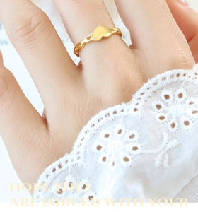 Vue détaillée d'une bague dorée ajourée avec un charm en cœur portée au doigt