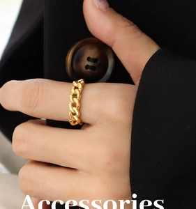 Close-up of golden Cuban chain ring worn by a model against a black suit background