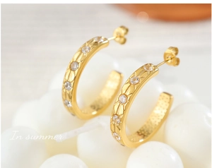 Macro view of 18K gold C-shaped earrings with starburst carvings and zircon stones