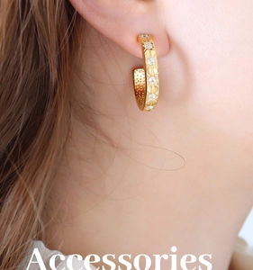 Close-up of 18K gold C-shaped earring with sparkling zircon starburst engravings