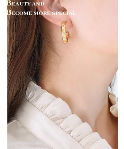 Close-up of a gold C-shaped earring with starburst engravings and zircon on ear