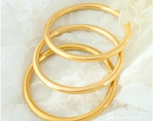 Three stackable minimalist matte gold-plated bangles displayed on white texture