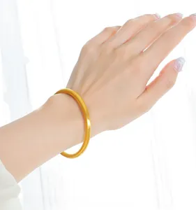 Close-up of a matte gold minimalist solid round bangle worn on the wrist in soft light