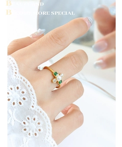 Detailed view of a gold-plated twisted ring featuring a white pearl and green gemstones