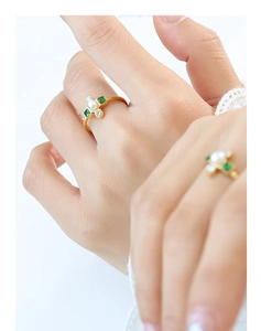 Detail of a gold plated ring with white pearl, green gems and spiral texture on hand