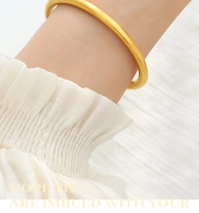 Close-up of a matte gold circular bangle worn by a model with elegant white ruffled sleeves