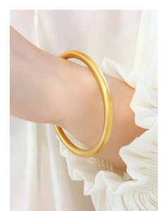 Close-up of a matte gold geometric bangle bracelet with a minimalist solid round design