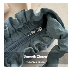Detailed macro view of a blue pleated fabric shoulder bag with a smooth metal zipper