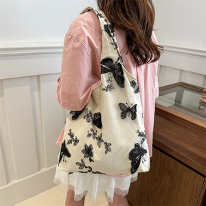 Off-white canvas tote bag featuring butterfly embroidery shown on a model's shoulder