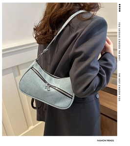 Detail of light blue denim crescent shoulder bag with metal zipper and adjustable strap