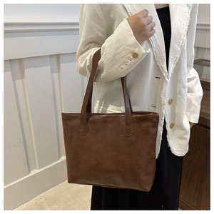 Brown tote bag with geometric stitching shown on model in white tweed jacket