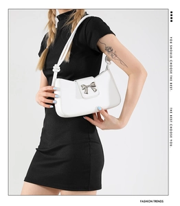 Close-up of a white shoulder bag with a silver metallic bow and stylish knotted strap