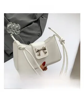 Detail view of white leather shoulder bag with silver bow ornament and knotted strap detail