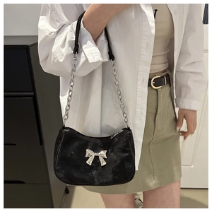 Detail of black PU leather shoulder bag with silver bow accent on female model