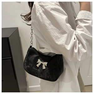 Close-up of black crescent shoulder bag with silver bow accent and chunky metal chain