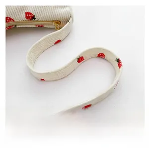 Gros plan sur la bandoulière en velours côtelé blanc avec motifs fraises et zip doré