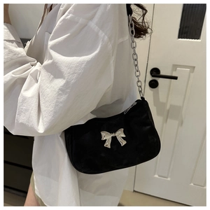 Detail of black shoulder bag featuring a silver bow accent and thick metal chain strap