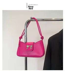 Detail view of rose red shoulder bag featuring silver metal bow and knotted strap design