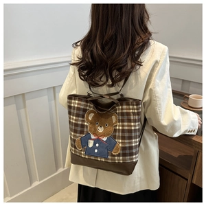 Détail du sac cabas à carreaux avec écusson d'ours porté par un mannequin en intérieur doux