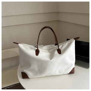 Close-up of white nylon tote bag with brown leather handles on a minimalist desk setup