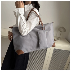 Detailed view of grey nylon tote bag with brown leather handles worn by a model