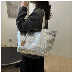 Detail of silver crocodile-patterned tote bag with metallic finish and decorative tag