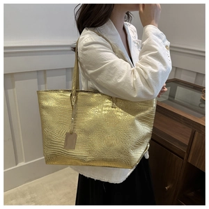 Detail of metallic gold tote bag with crocodile texture worn by a model in a studio