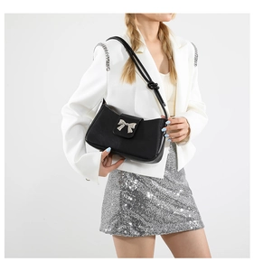 Detail of black faux leather shoulder bag with silver butterfly hardware on model