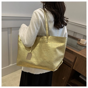 Detail shot of a shiny gold tote bag with crocodile pattern and thin shoulder strap