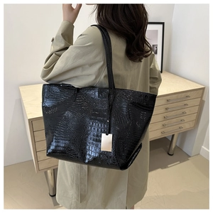Detail of black crocodile texture tote bag with silver charm on model in trench coat